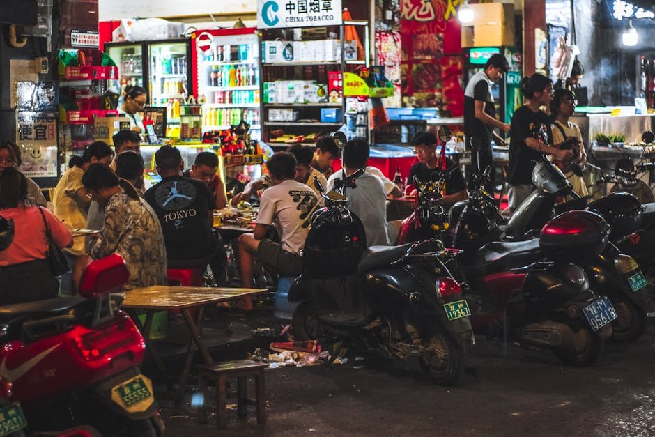 Bustling Asian street market with diners and motorbikes at night.
